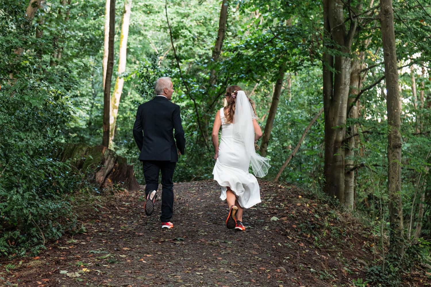 Wedding couple walking hand in hand through a serene wooded path.
