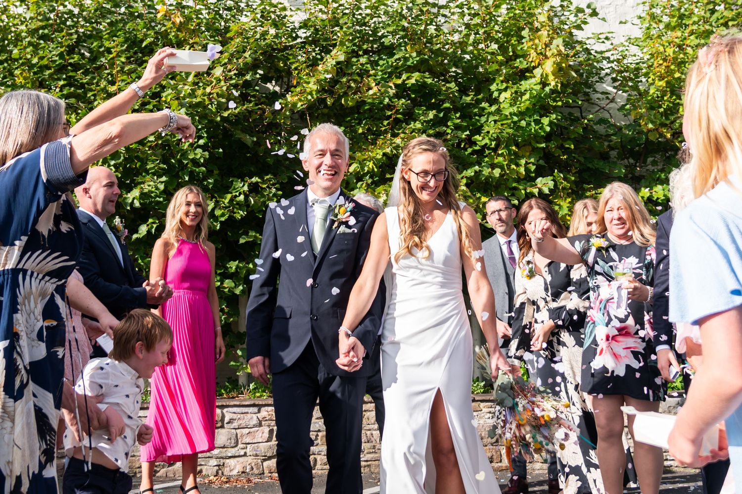 Wedding guests celebrate outdoors in garden setting with bright summer foliage.