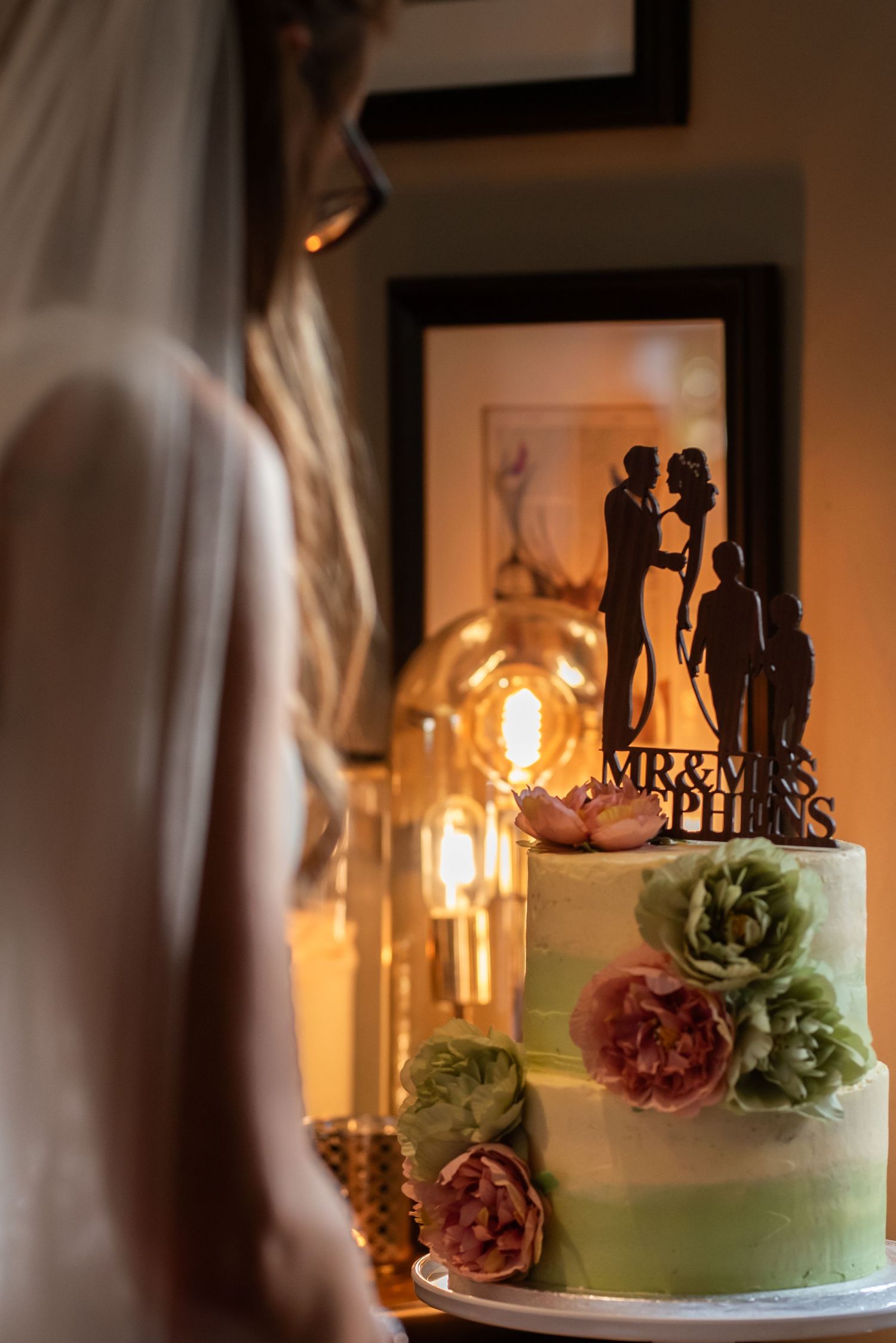 Wedding cake display with soft lighting and silhouette cake topper decoration.