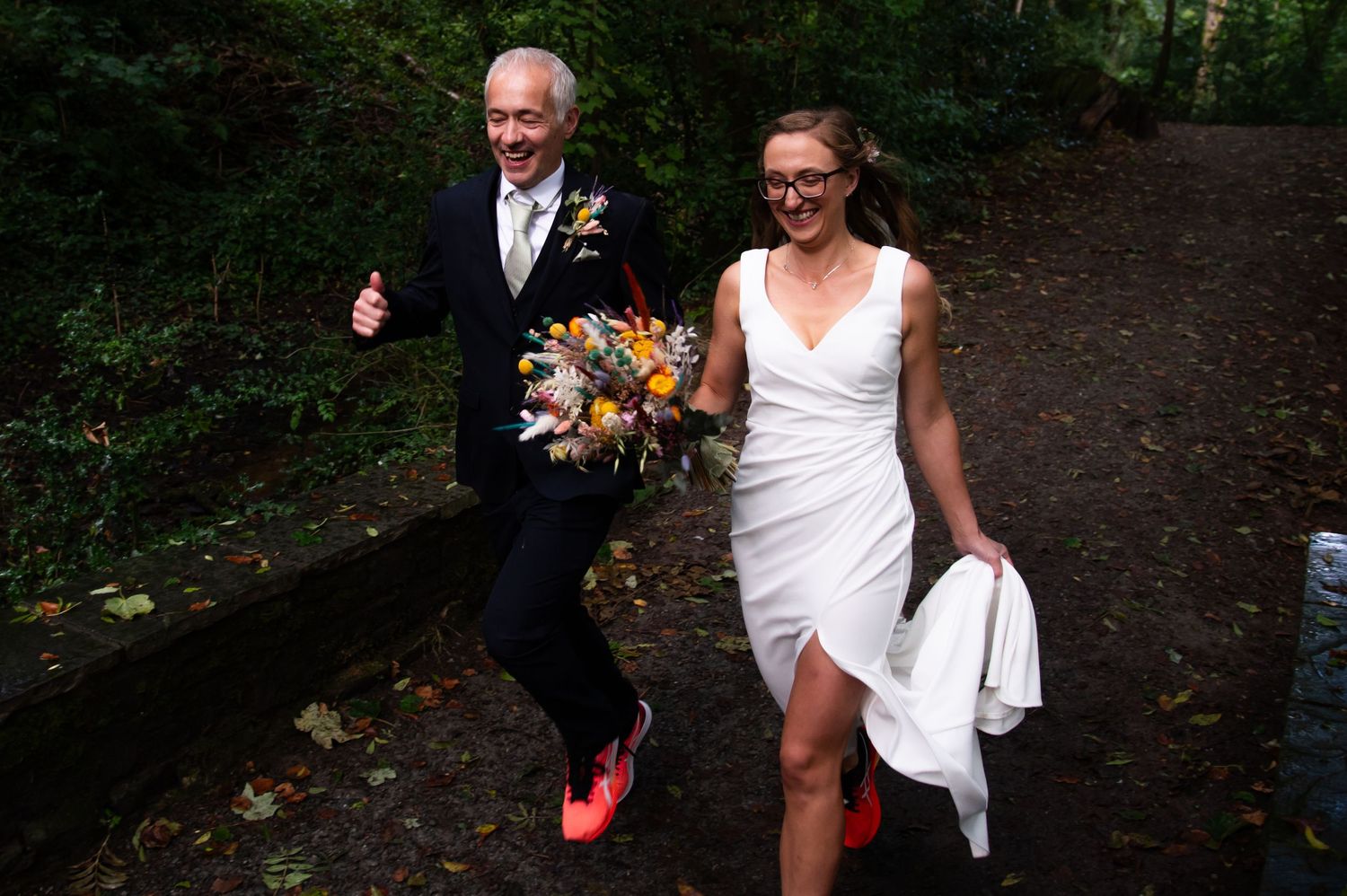 Joyful wedding couple laughs together on rustic wooden bridge surrounded by greenery.