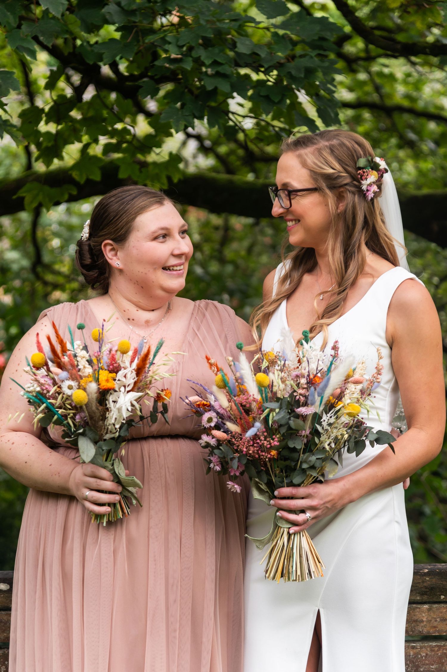 Bridesmaids in pink dresses hold colorful wildflower bouquets outdoors.