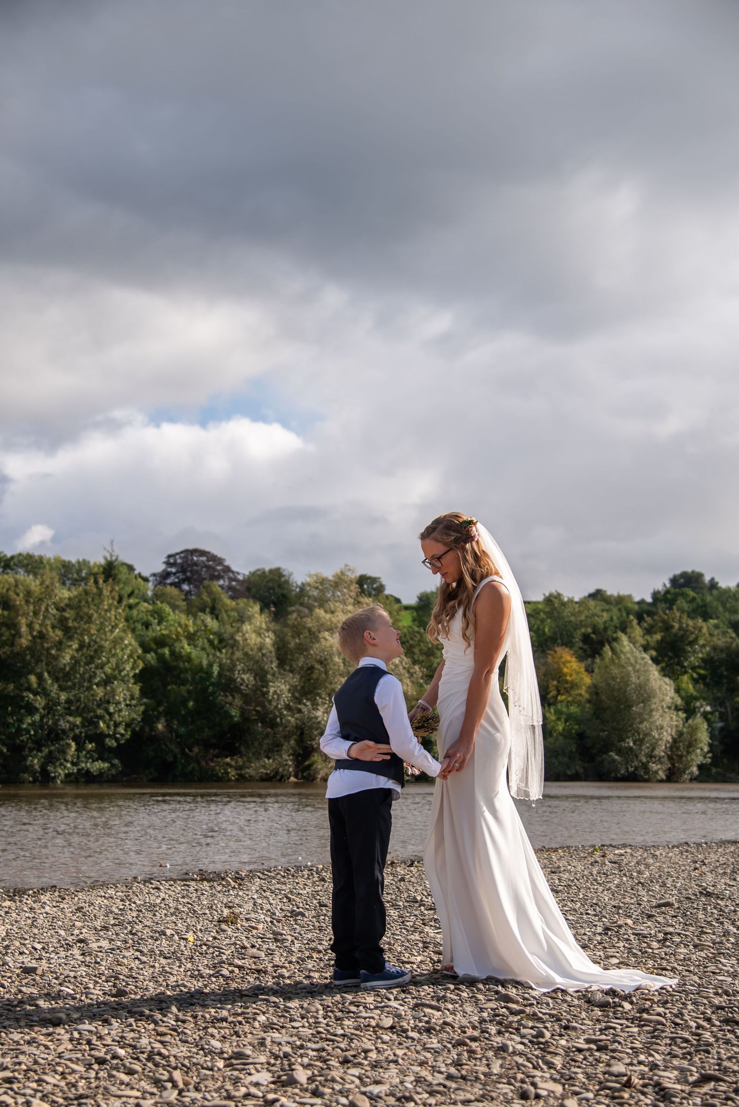 Wedding photo session on rocky riverbank under dramatic cloudy sky.