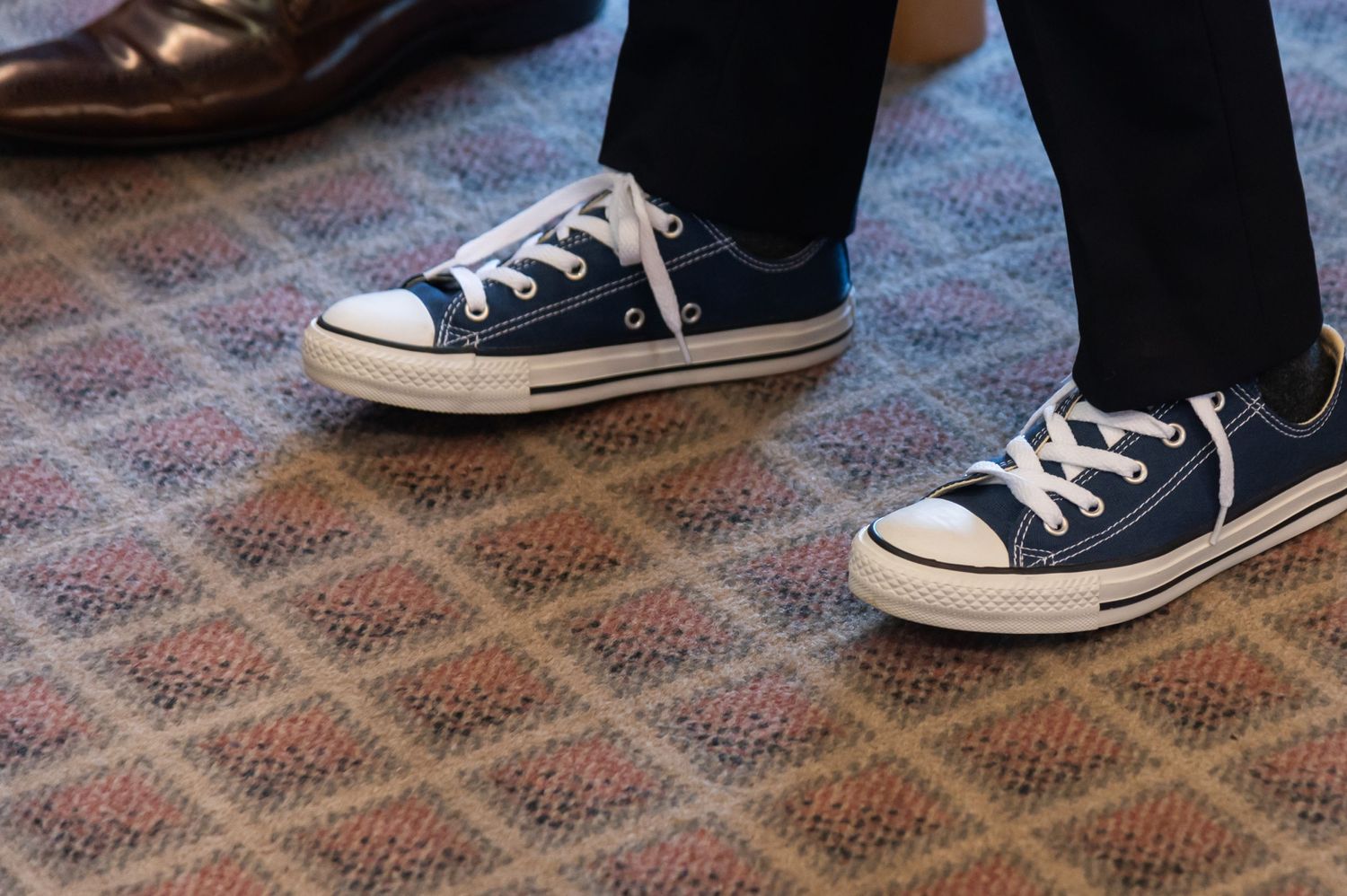 Row of classic blue Converse sneakers on patterned carpet.
