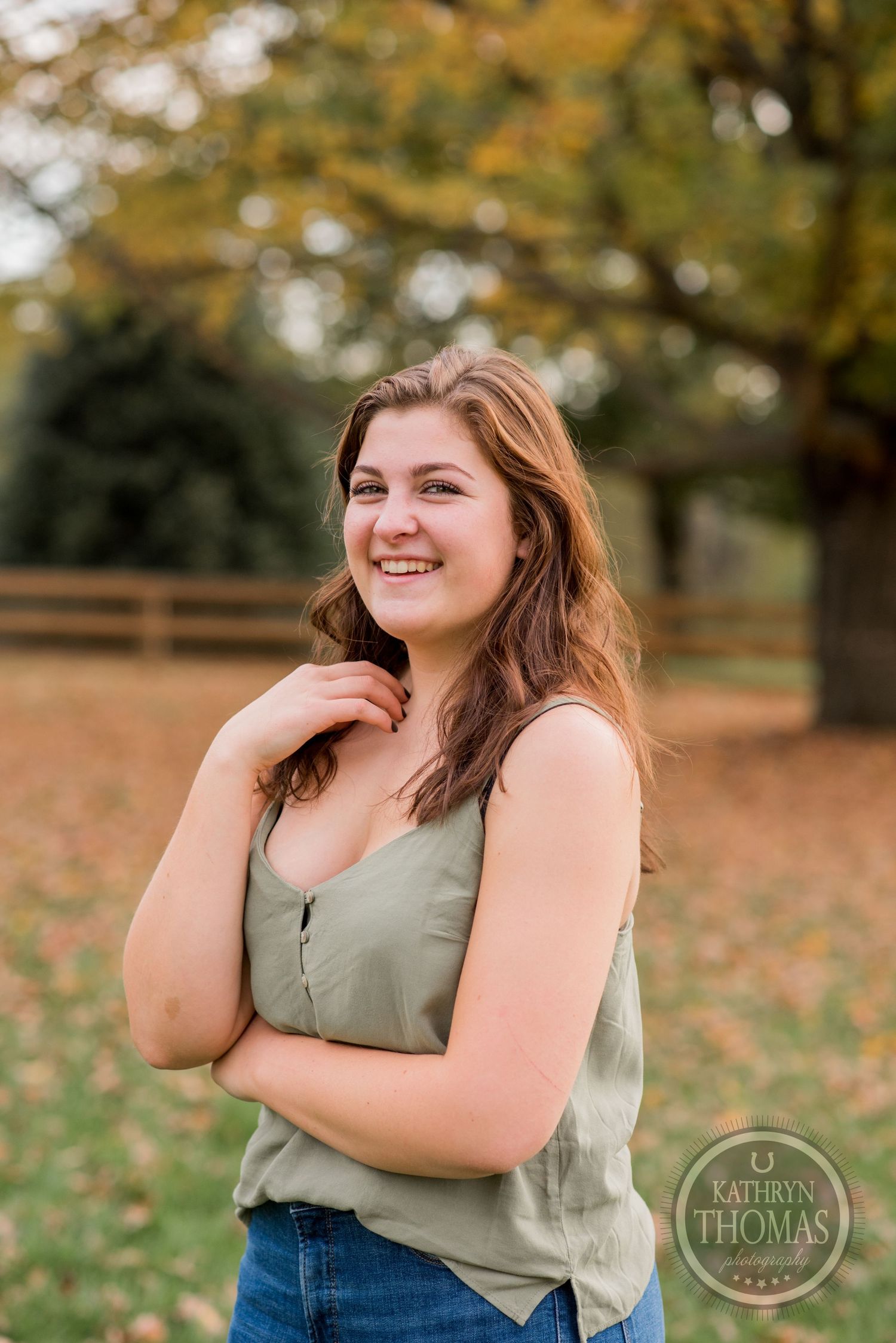 Casual outdoor portrait against autumn trees and wooden fencing.