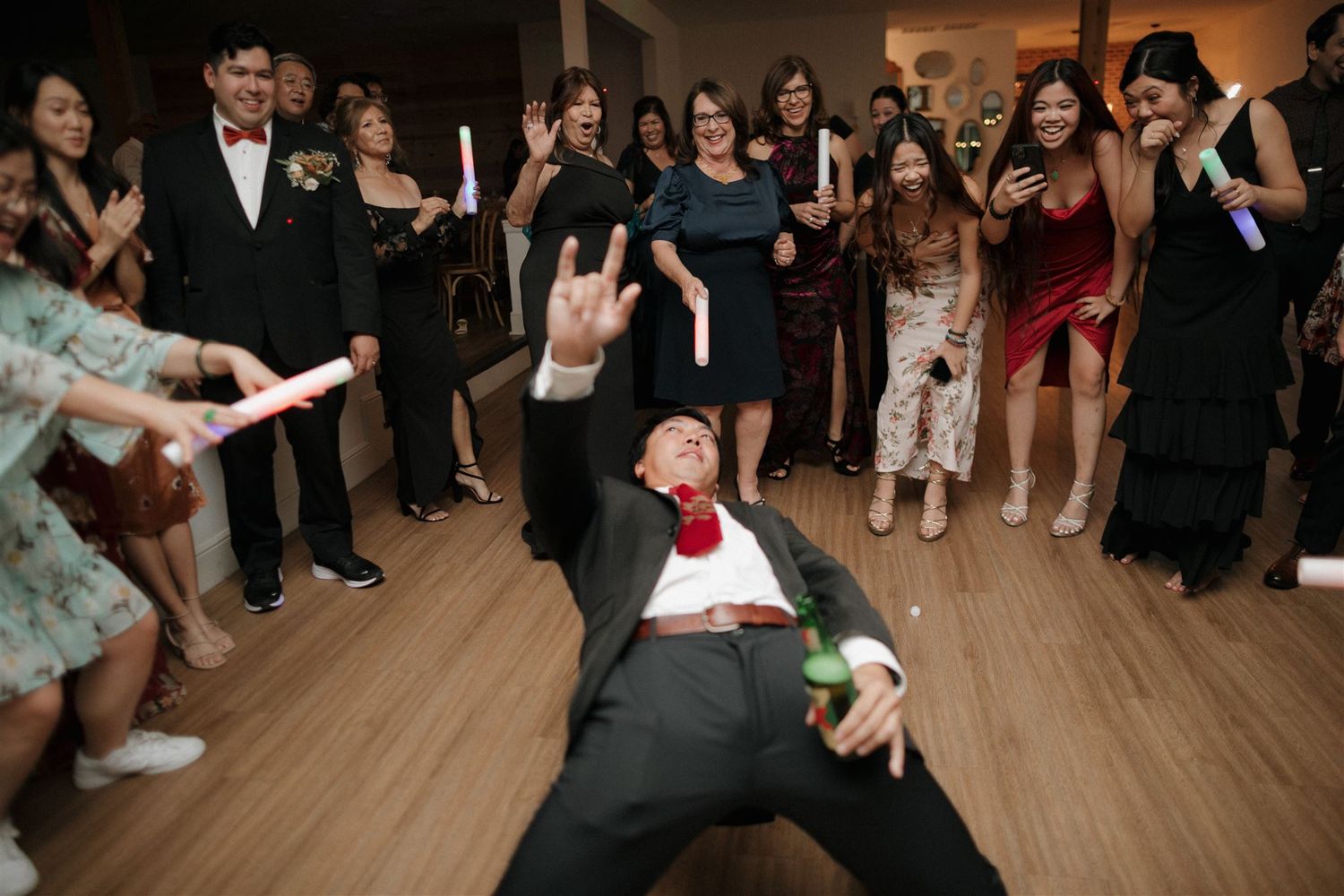 Wedding guests cheer as a guest performs an energetic dance move on the reception dance floor.