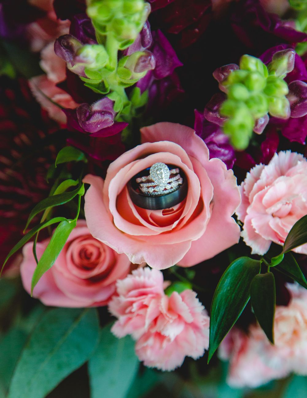 Wedding rings nestled inside a pink rose surrounded by colorful floral bouquet arrangement.