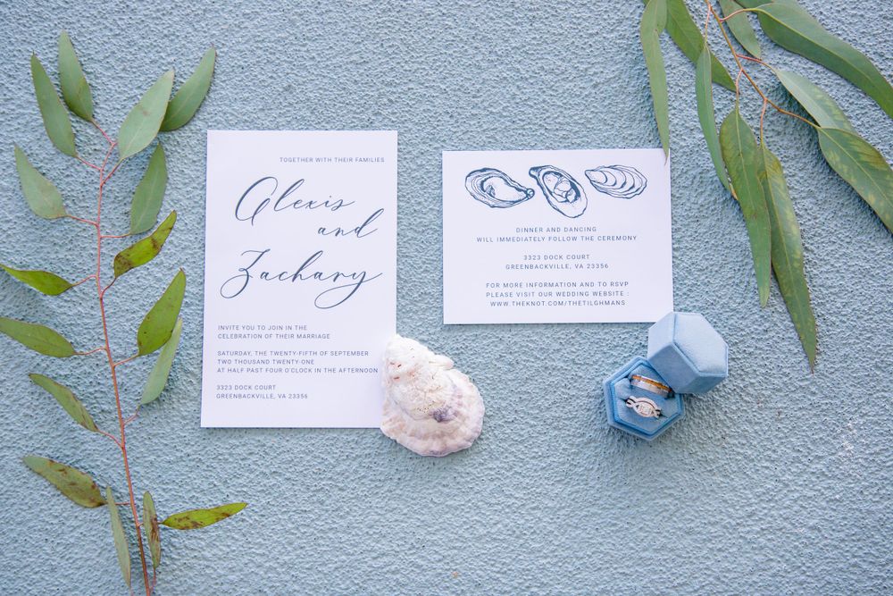Elegant wedding invitation suite for Alexis and Zachary displayed with greenery and blue ring box.