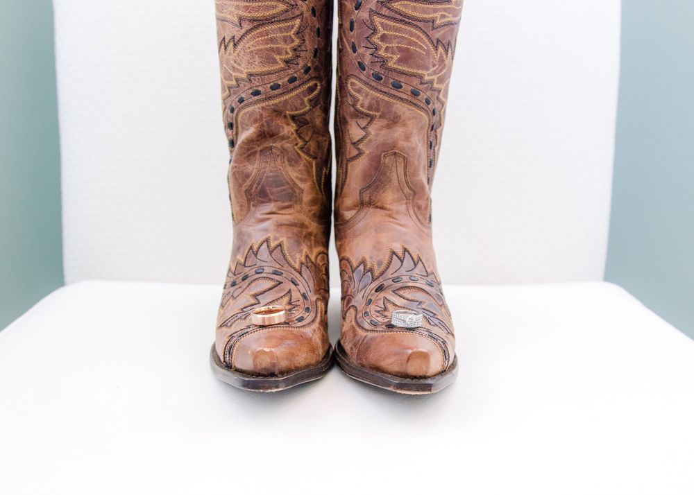 Detailed brown leather cowboy boots with intricate tooled floral pattern on white surface.