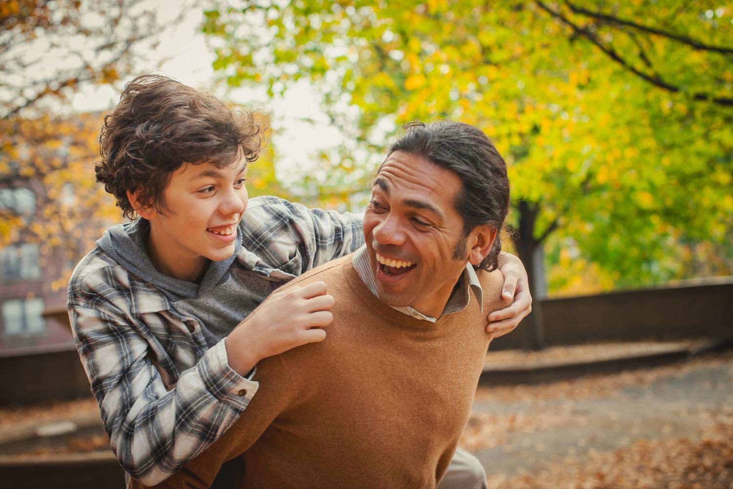 Two people laughing and embracing outdoors during autumn.