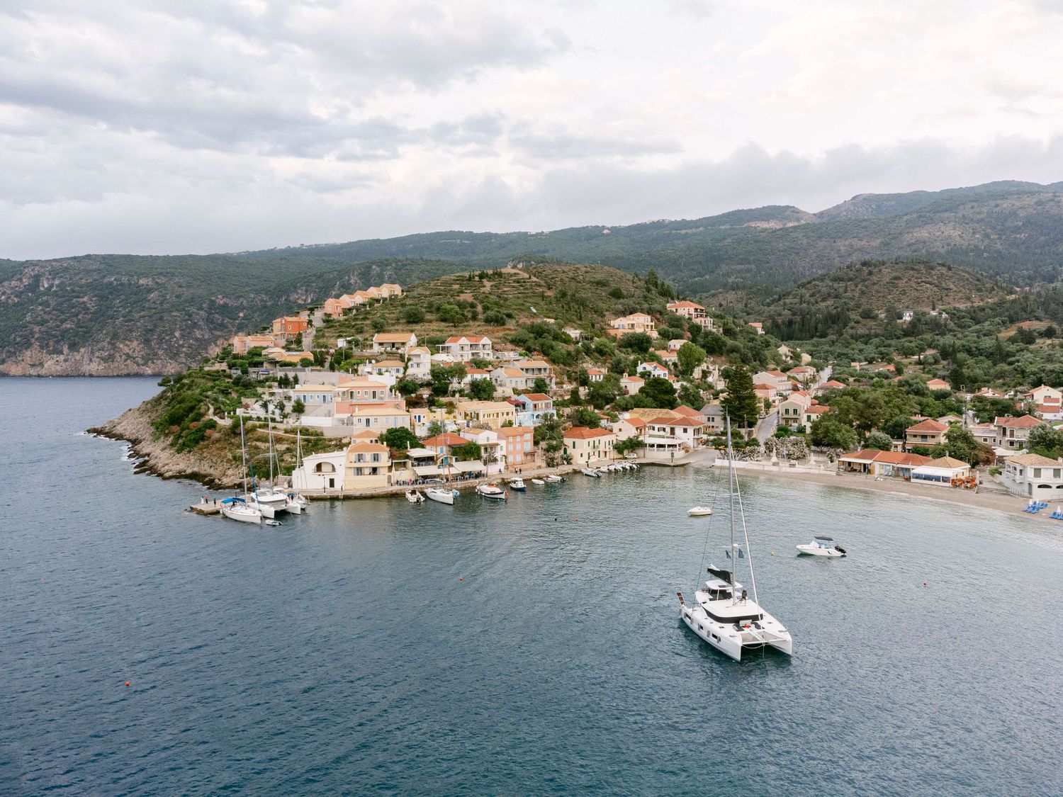 Aerial view of a coastal Mediterranean village with boats anchored in turquoise waters.