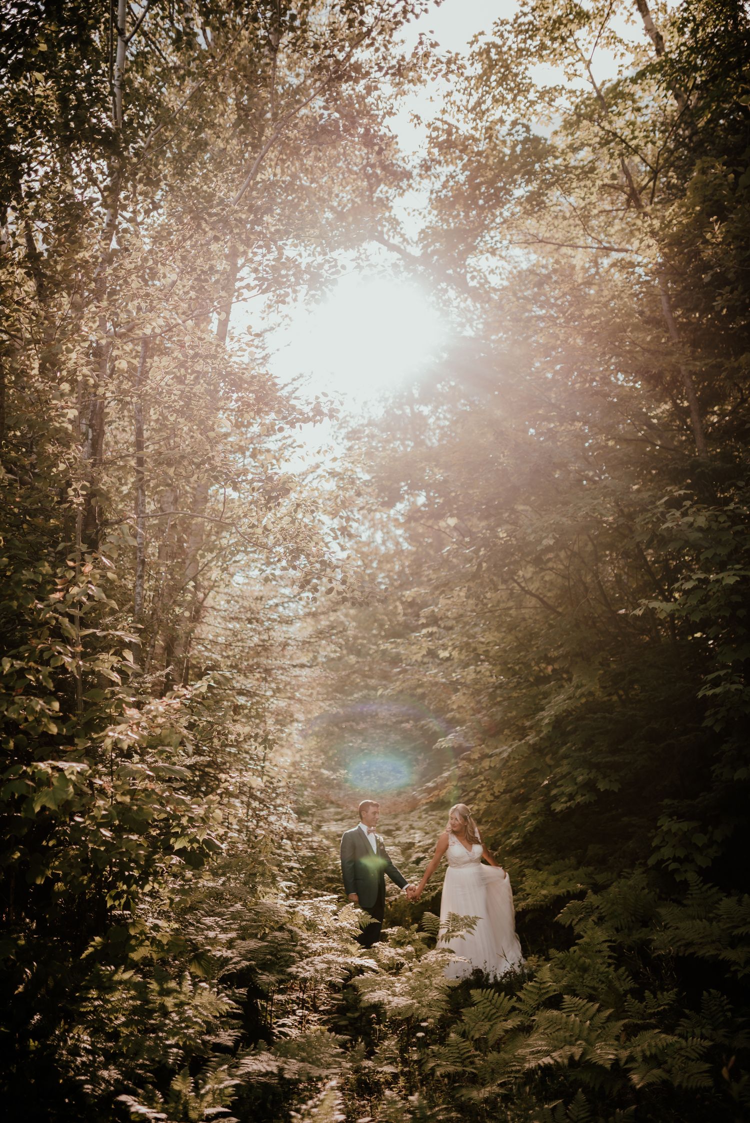 Two figures in white walking through a sunlit forest path with dreamy golden light filtering through the trees.
