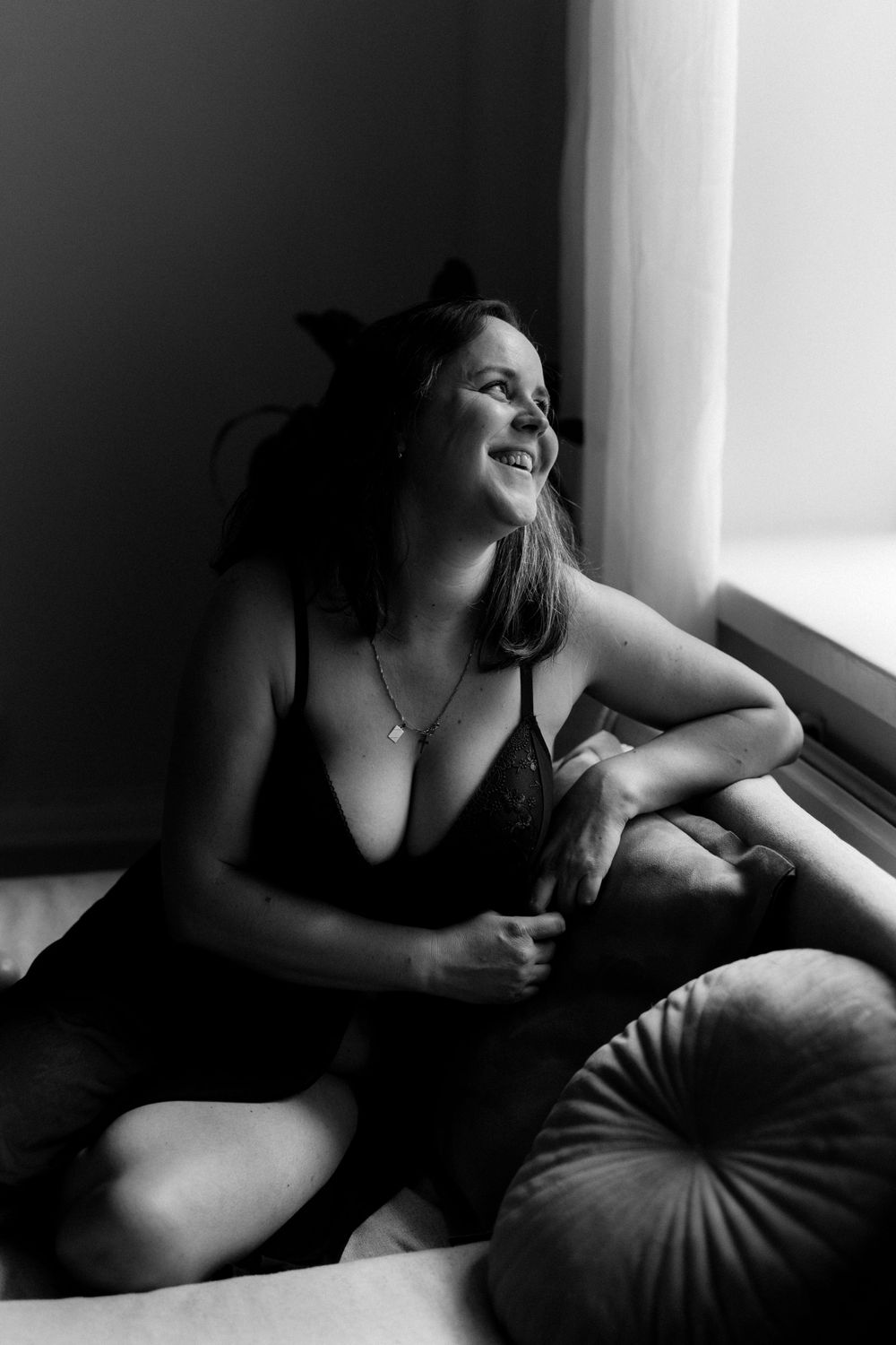 Mustavalkoinen boudoirvalokuva naisesta sohvalla ikkunan edessä