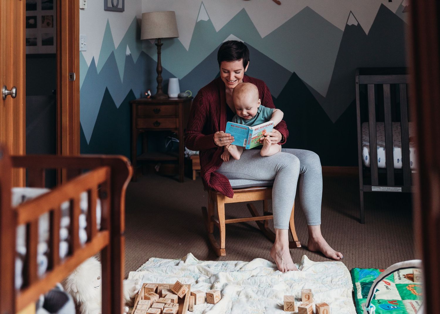 Nursery room with mountain mural wall art and rocking chair in soft lighting.