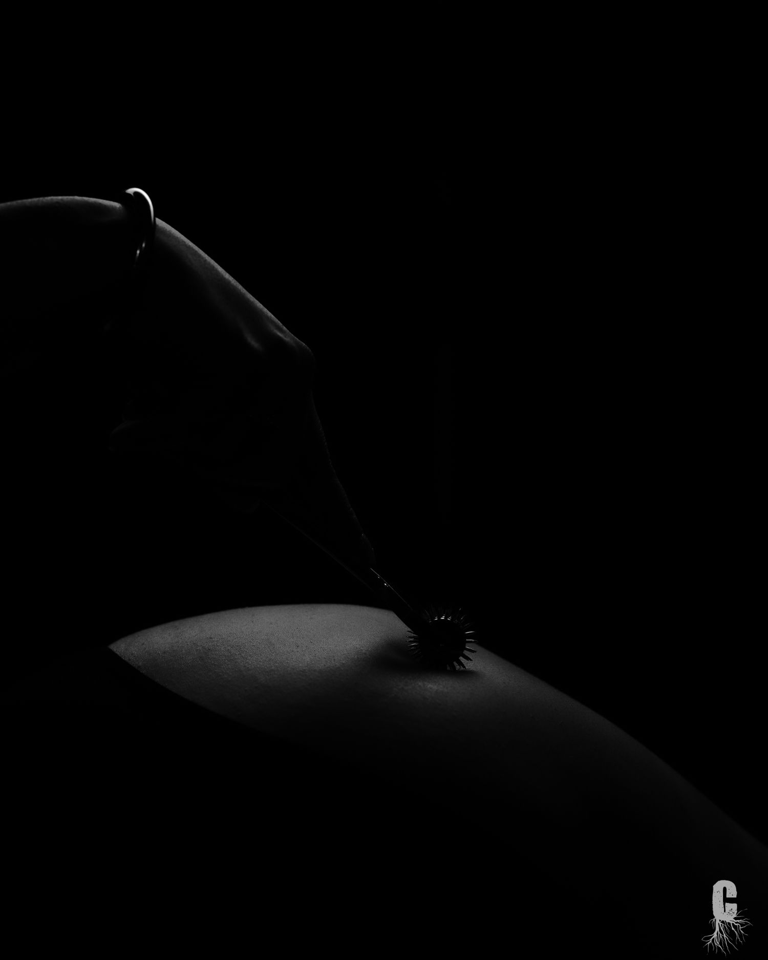 A dark body scape photo of a model dragging a pinwheel across her butt