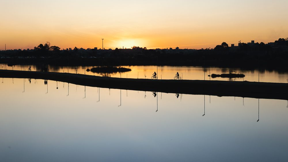 Sunset over calm lake with soft orange sky reflecting on still water.