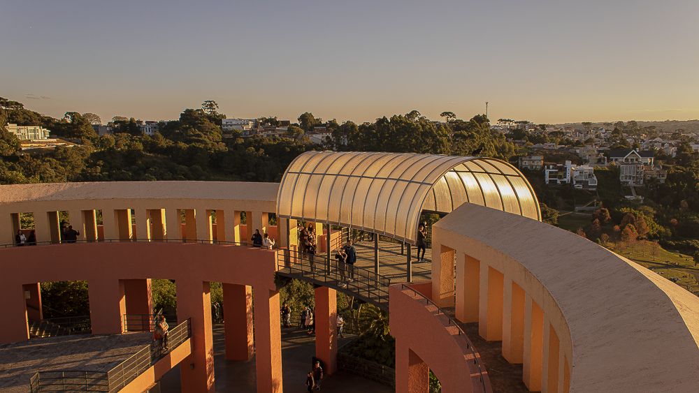 Curved architectural terrace with glass canopy at sunset.