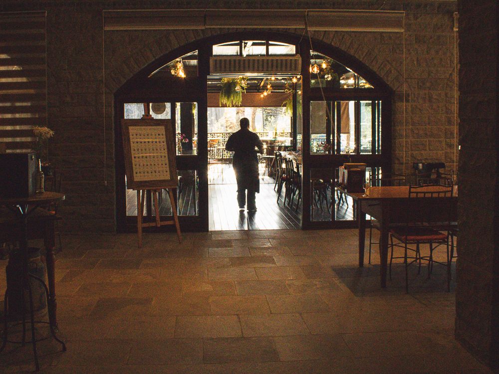 Silhouetted waiter walking through warmly lit restaurant entrance, photographed by Piret Victoria Ribas.