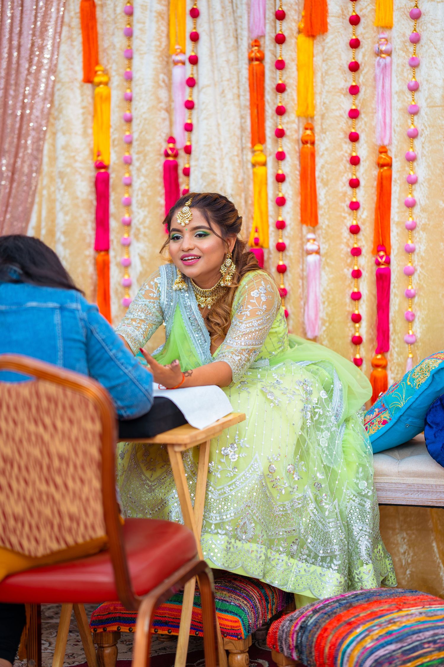 Person in sparkly mint green lehenga smiles during pre-wedding celebration with festive decor.