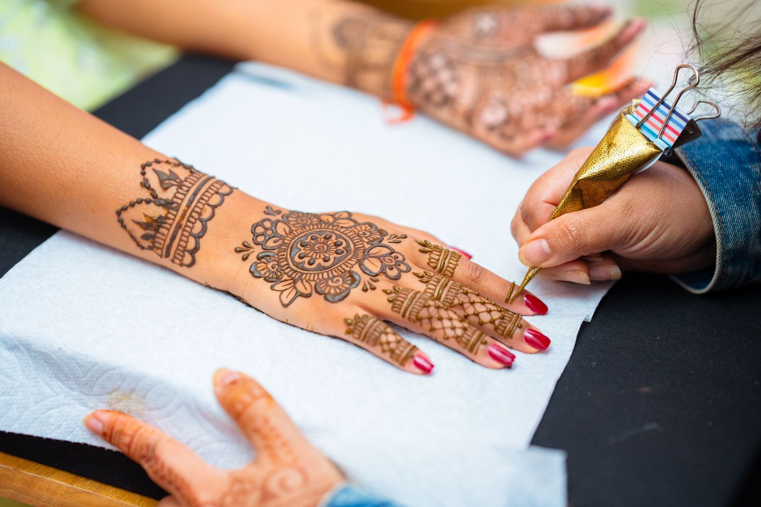 Close-up of intricate henna design being applied to hand during traditional Indian wedding ceremony.