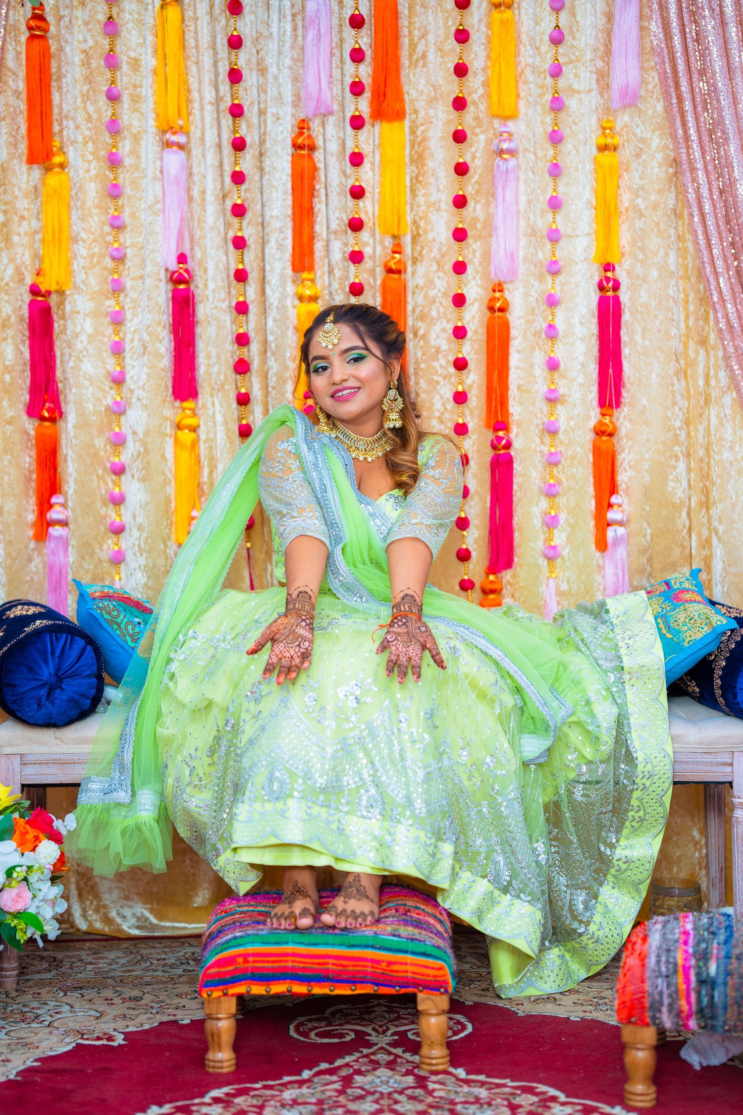 Person in mint green lehenga sits gracefully on footstool during wedding celebration.