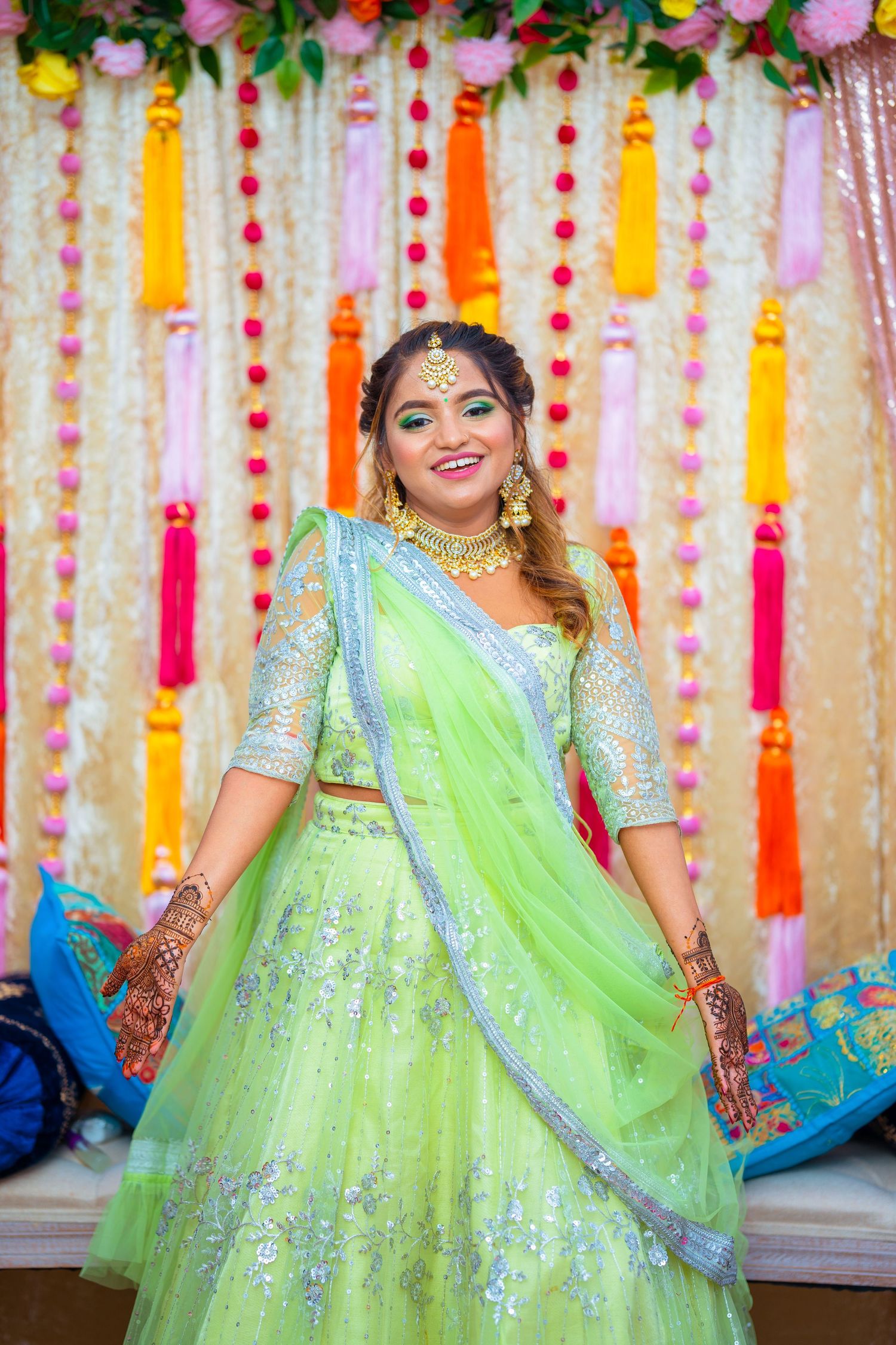 Person poses in elegant mint green and silver embroidered lehenga against vibrant floral backdrop.