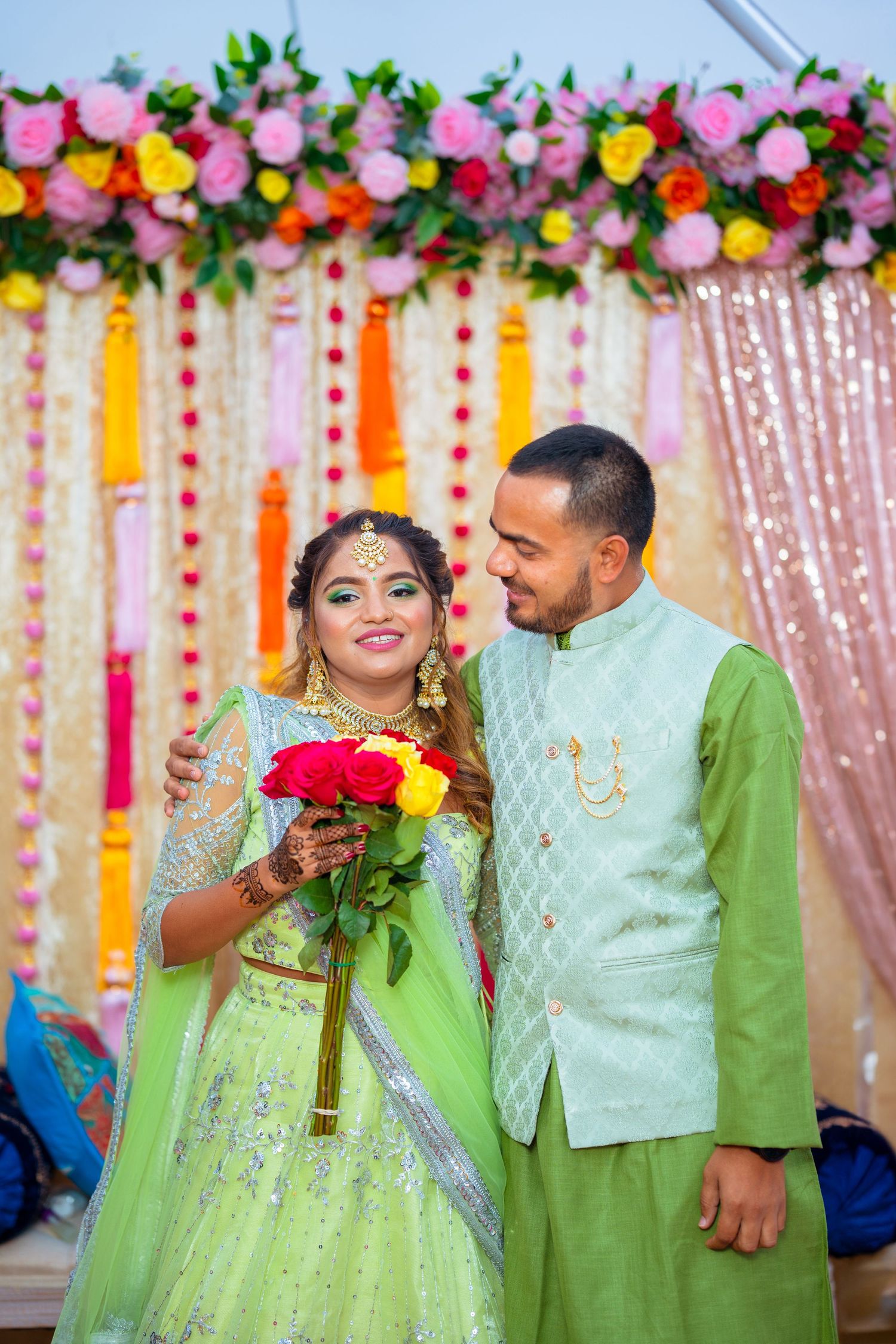 Couple in coordinating mint green outfits pose with red roses against colorful backdrop.
