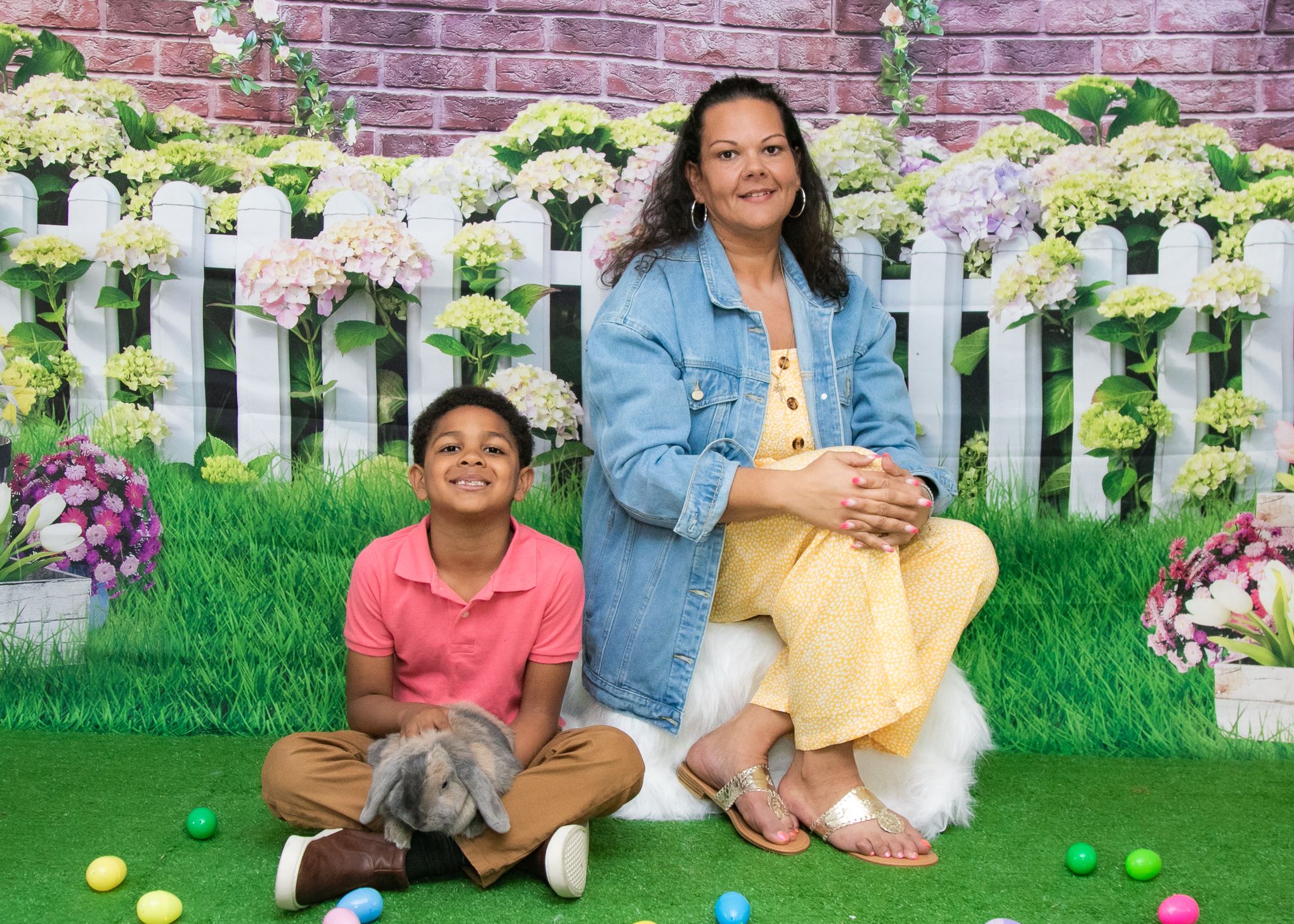 People pose with a bunny against a garden backdrop with white picket fence and floral decorations.