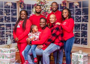 Holiday family portrait with matching red outfits in front of decorated Christmas backdrop.