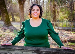 Woman in emerald green ruffle sleeve sweater poses outdoors on wooden bench.