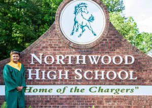 A student poses in front of the Northwood High School sign with mascot logo.