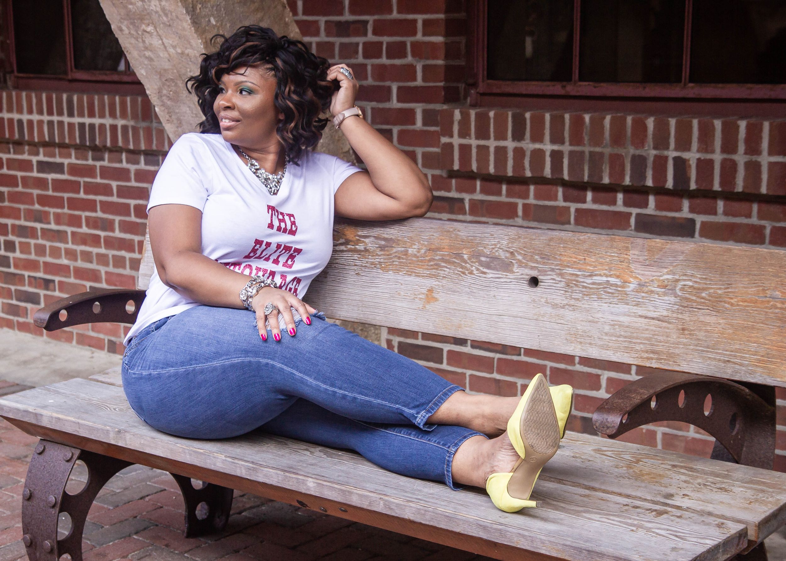 Casual outdoor portrait on wooden bench against brick building backdrop.