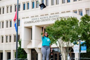 A graduate celebrates with cap toss in front of Cumberland County Courthouse.