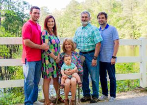 A multi-generational family poses together by a white fence in casual spring attire.
