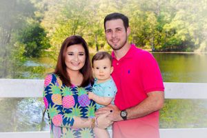 A young family in bright spring clothes poses together against a scenic backdrop.