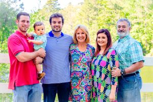 Multi-generational family poses together outdoors in colorful clothing on a sunny day in nature.
