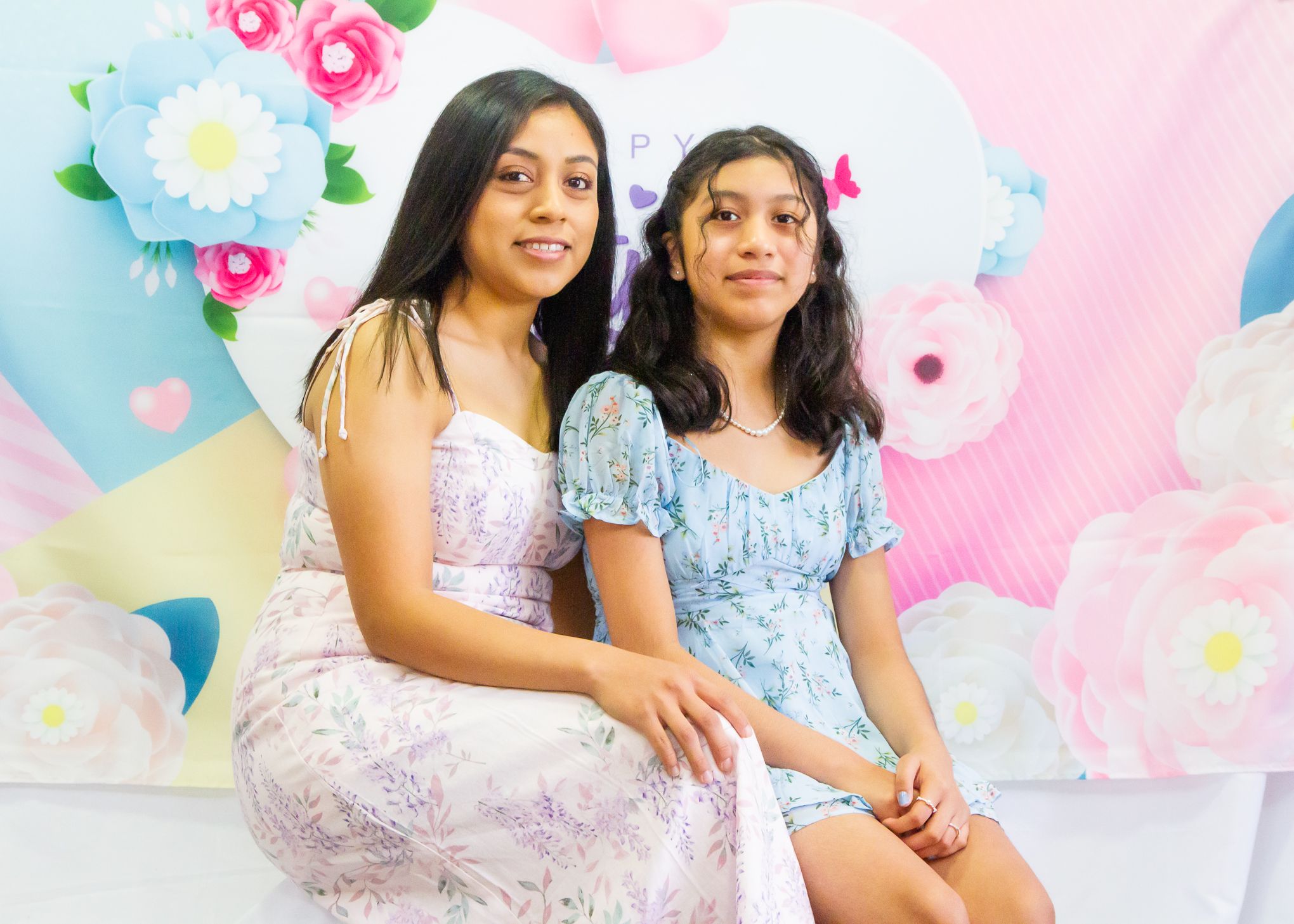 Two people pose together in front of decorative pink and blue floral backdrop.