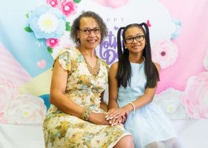 Two people sit together against a pastel floral backdrop for a spring portrait.