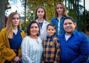 Family group portrait against autumn trees wearing coordinated blue and plaid outfits.