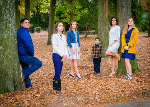 Group photo on autumn leaves against large tree trunks in outdoor setting.