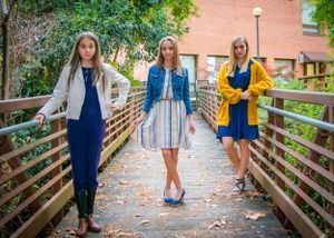 Three women in coordinating blue and yellow outfits pose on wooden bridge during fall.