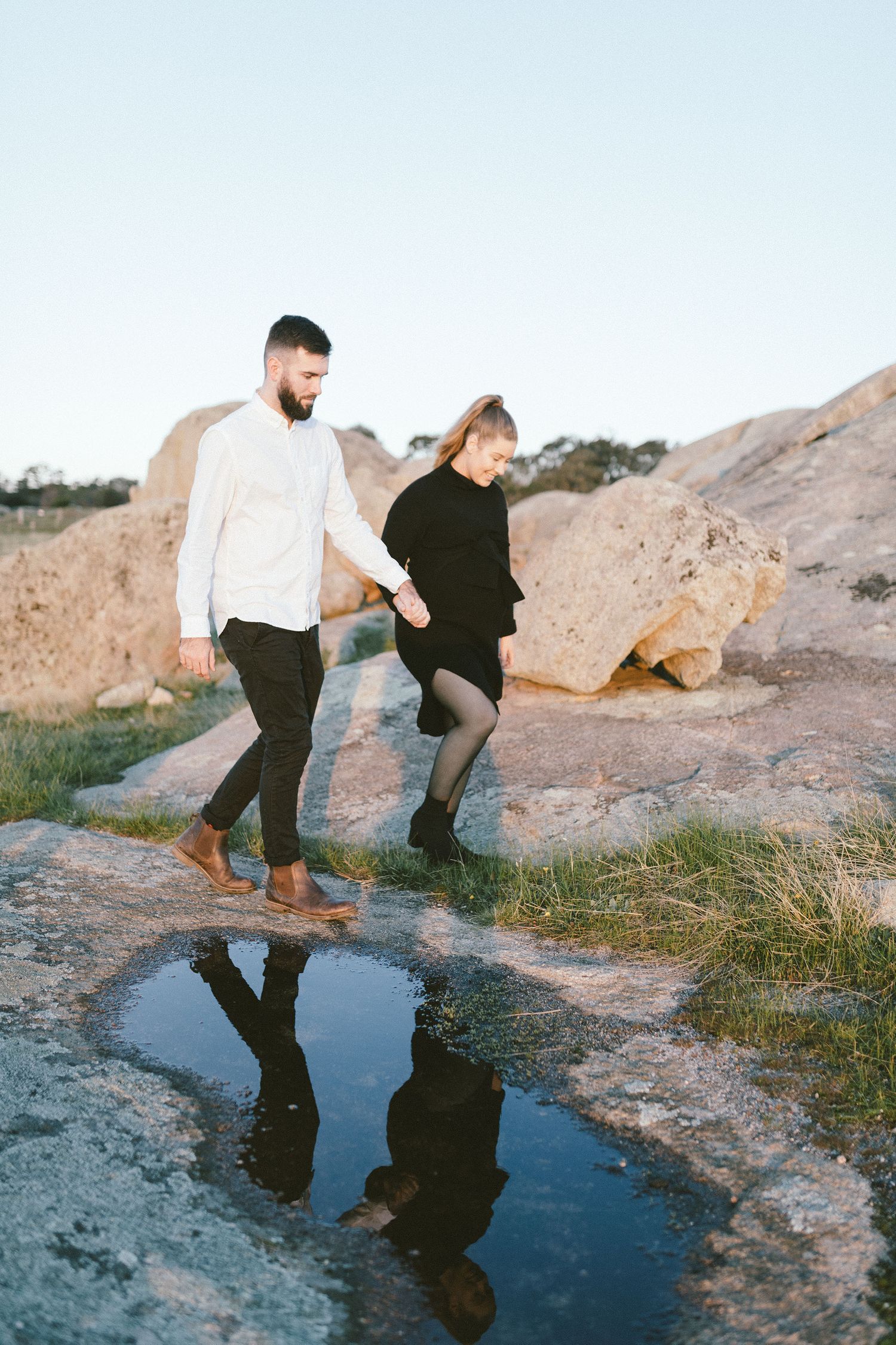 Couple walking near a puddle reflecting their silhouettes on rocky terrain.