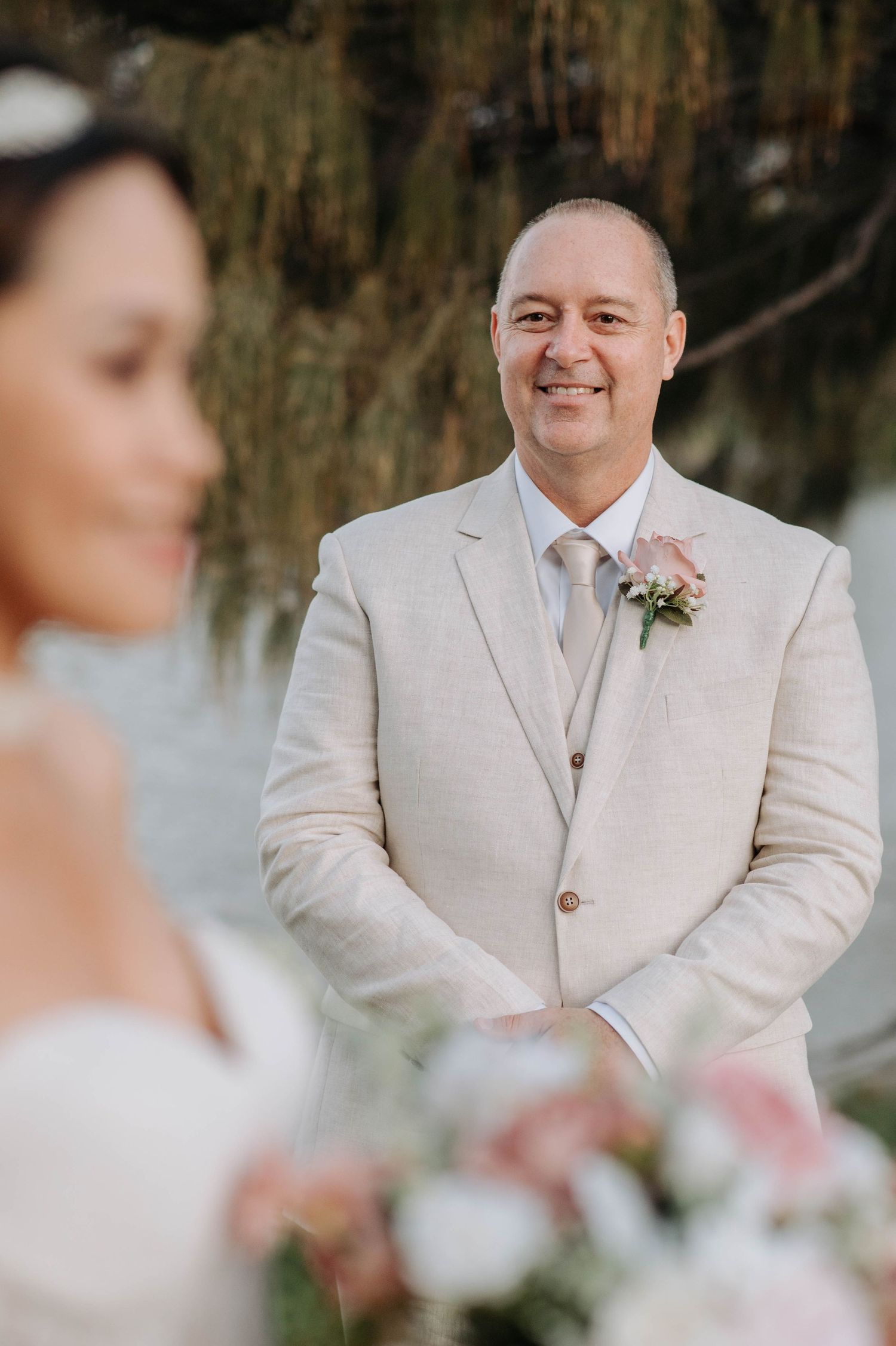 Wedding portrait showcasing groom in light beige suit with pink boutonniere.