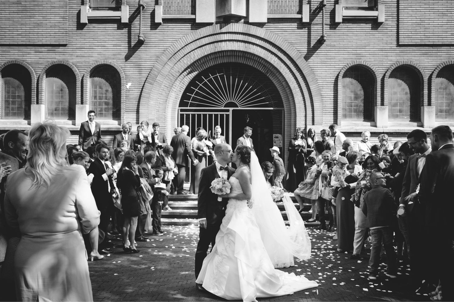 Wedding guests throw confetti as newlyweds exit historic brick church building.