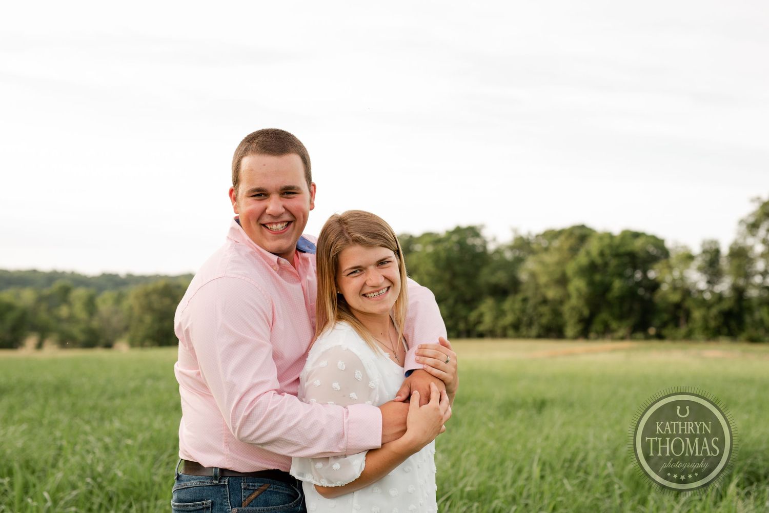 A couple embraces while standing in a sunny green field.