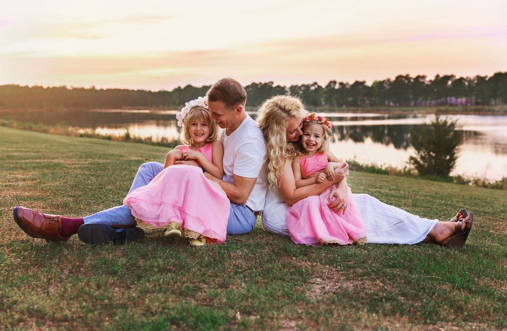 Family members relaxing on grass during golden hour near a serene lake.