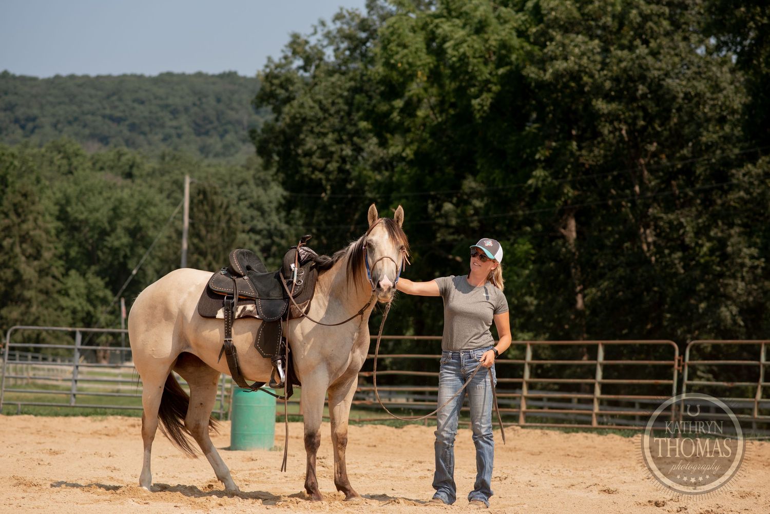 Two horses being prepped for riding in outdoor arena with mountains visible.