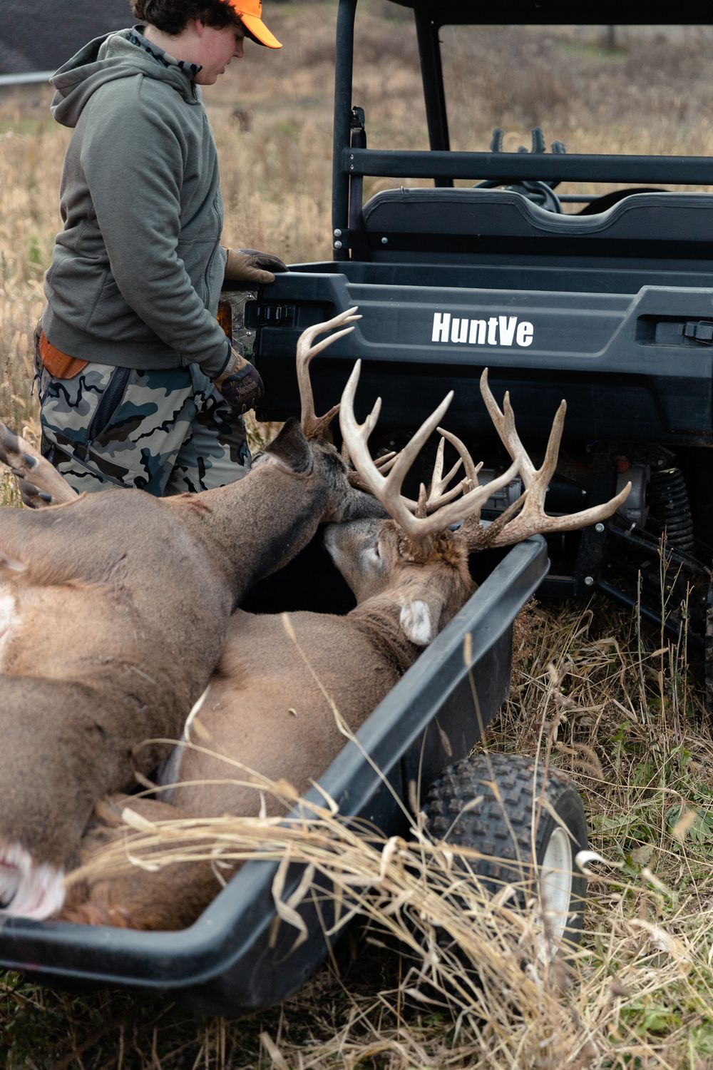 two large whitetail buck in trailer getting pulled behind UTV with boy standing next to trailer