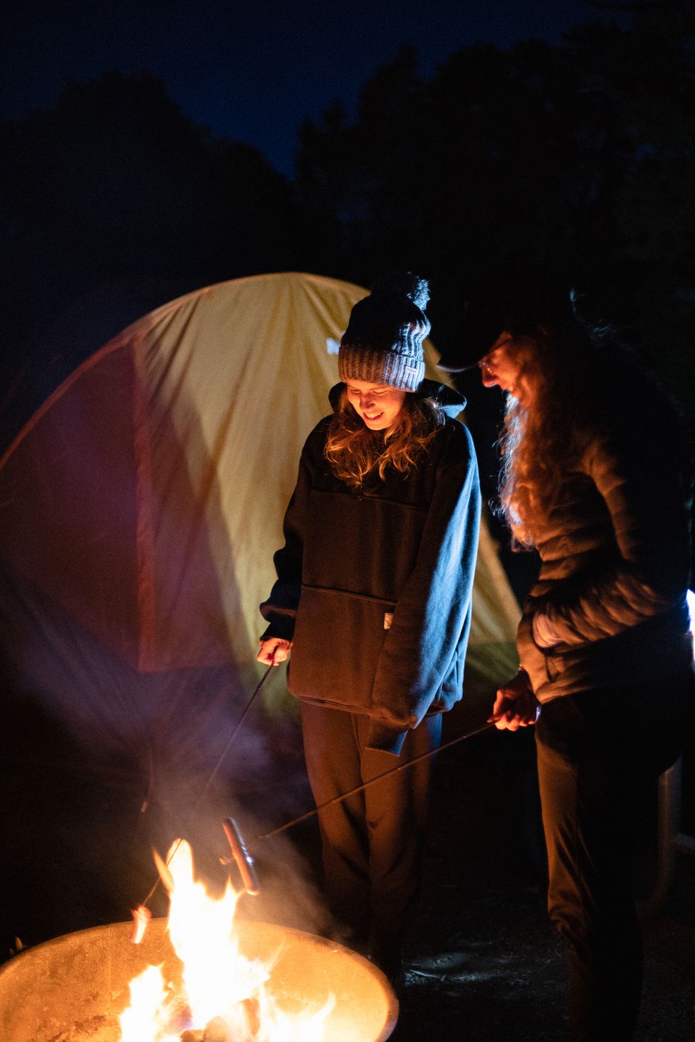 two girls standing close to a fire with orange light reflecting onto their clothing and faces