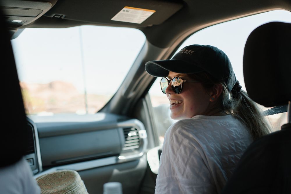 girl sitting in passenger seat smiling at driver of car with sunglasses and hat on