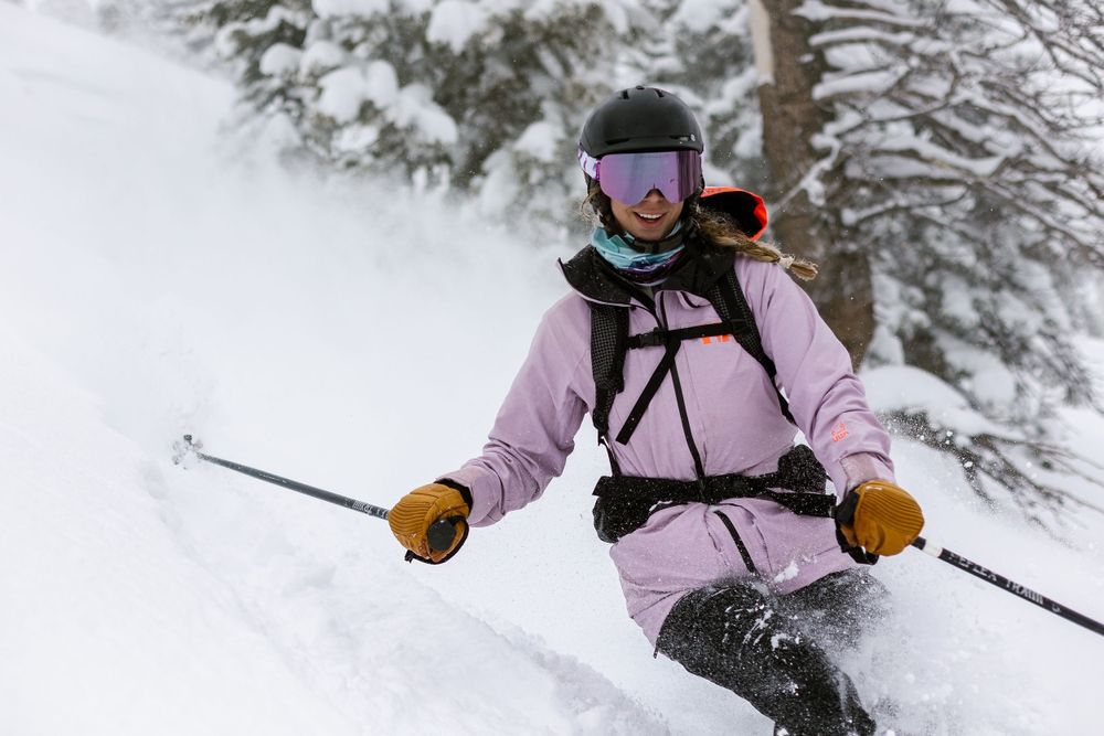 woman skiing in snow wearing pink ski jacket smiling at camera